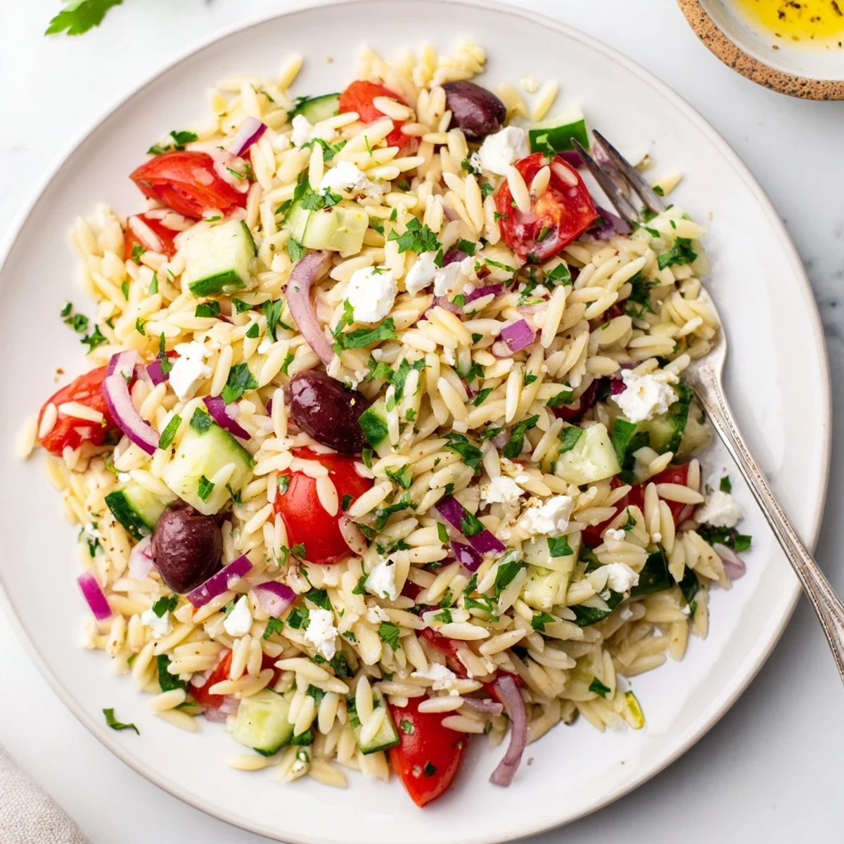 A vibrant Greek Orzo Salad with cherry tomatoes, cucumber, and feta tossed in a zesty lemon dressing.