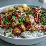 Steaming teriyaki chicken and rice bowl with crisp vegetables and caramelized pineapple chunks.