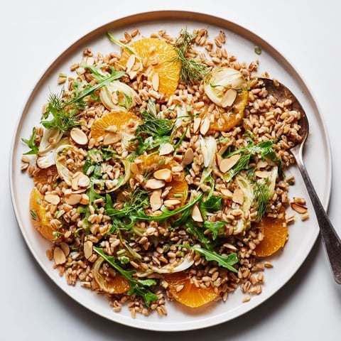 Farro salad with fennel, oranges, and almonds glistens with citrus vinaigrette on a rustic wooden table.