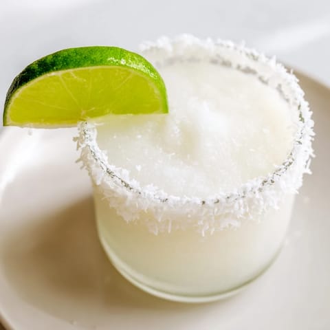 A frosty White Christmas Margarita slush, beautifully garnished with lime wedge and coconut flakes.