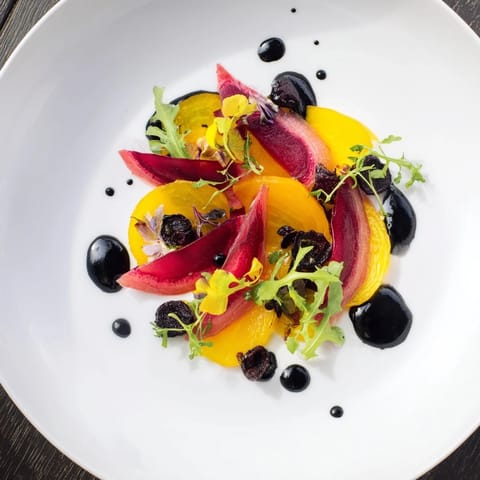 Elegantly plated The Shadow Play: A dark and vibrant vegetarian starter with layered golden beets and black tahini.