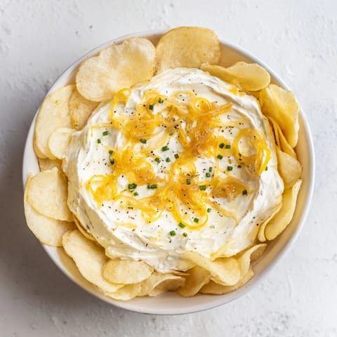 A close-up of a serving bowl filled with creamy onion dip, perfect with salty potato chips.