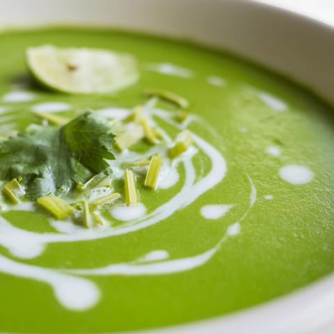 A close-up of vibrant green Spinach Coriander Lemongrass Soup with a swirl of coconut milk.  