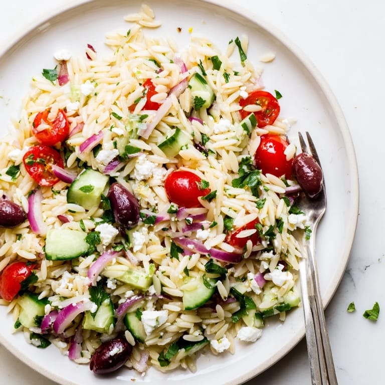 A chilled Greek Orzo Salad with tender pasta, crisp veggies, and fresh herbs, ready to serve.