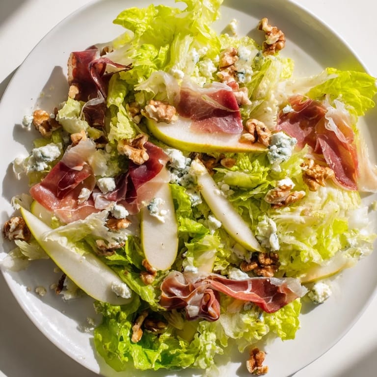 A close-up of pear wedges, creamy blue cheese, and crispy prosciutto on frisée leaves, ready for a light lunch.