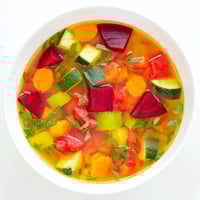 A steaming bowl of Rainbow Vegetable Detox Soup, brimming with colorful chunks of beetroot, carrots, and fresh green herbs.