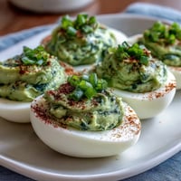 Creamy green avocado deviled eggs garnished with fresh herbs, perfect for spring parties and healthy snacking.  